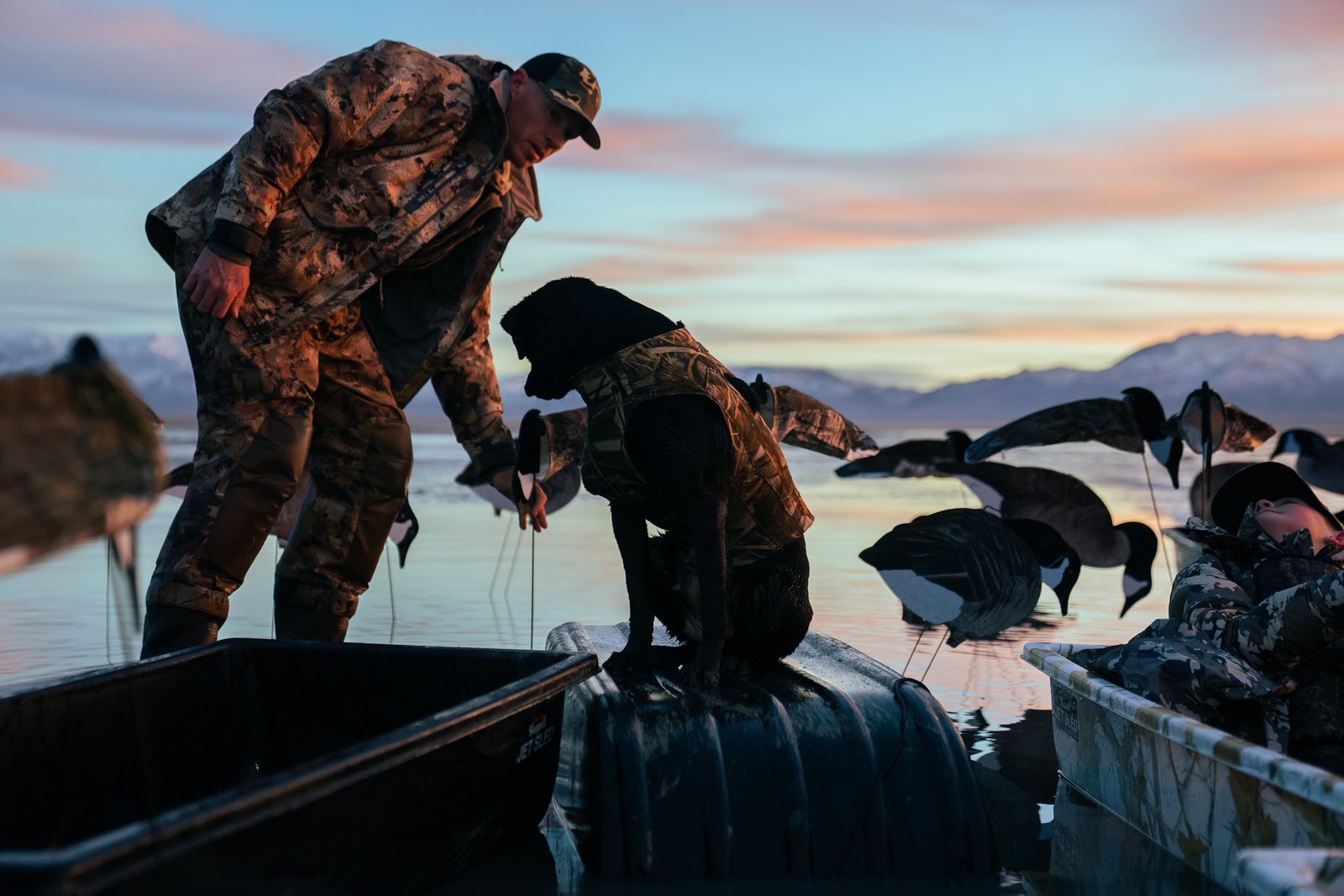 A hunter and black Labrador in a marsh at sunrise
